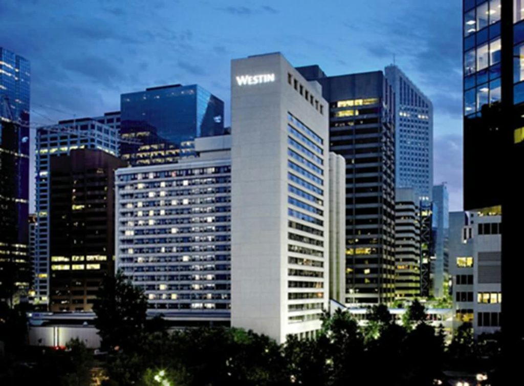 A downtown hotel frontage with its canopy over the entrance and office towers rising behind it.